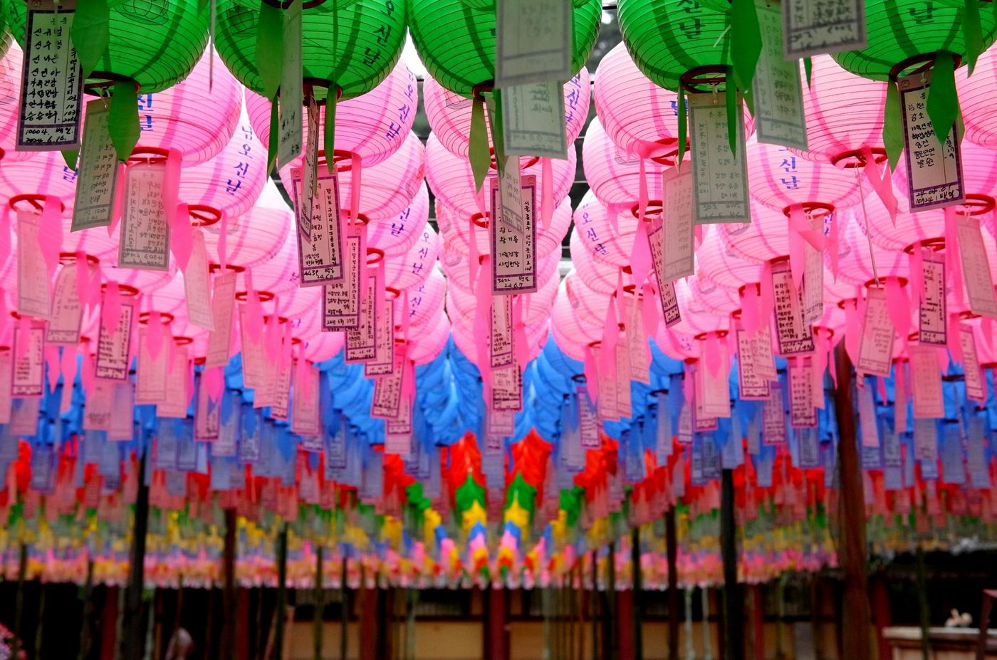 Roze, groene en blauwe lantaarns met wensbriefjes onder het dak van een boeddhistische tempel