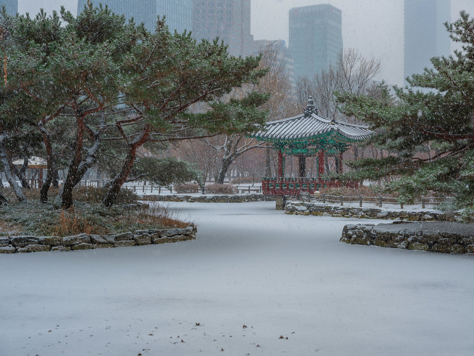 Traditioneel paviljoen in een besneeuwd park in Seoul met wolkenkrabbers op de achtergrond